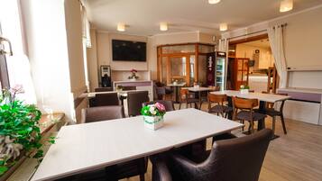 A modern dining area with tables and chairs, a flat-screen TV mounted on the wall, and a visible kitchen area.