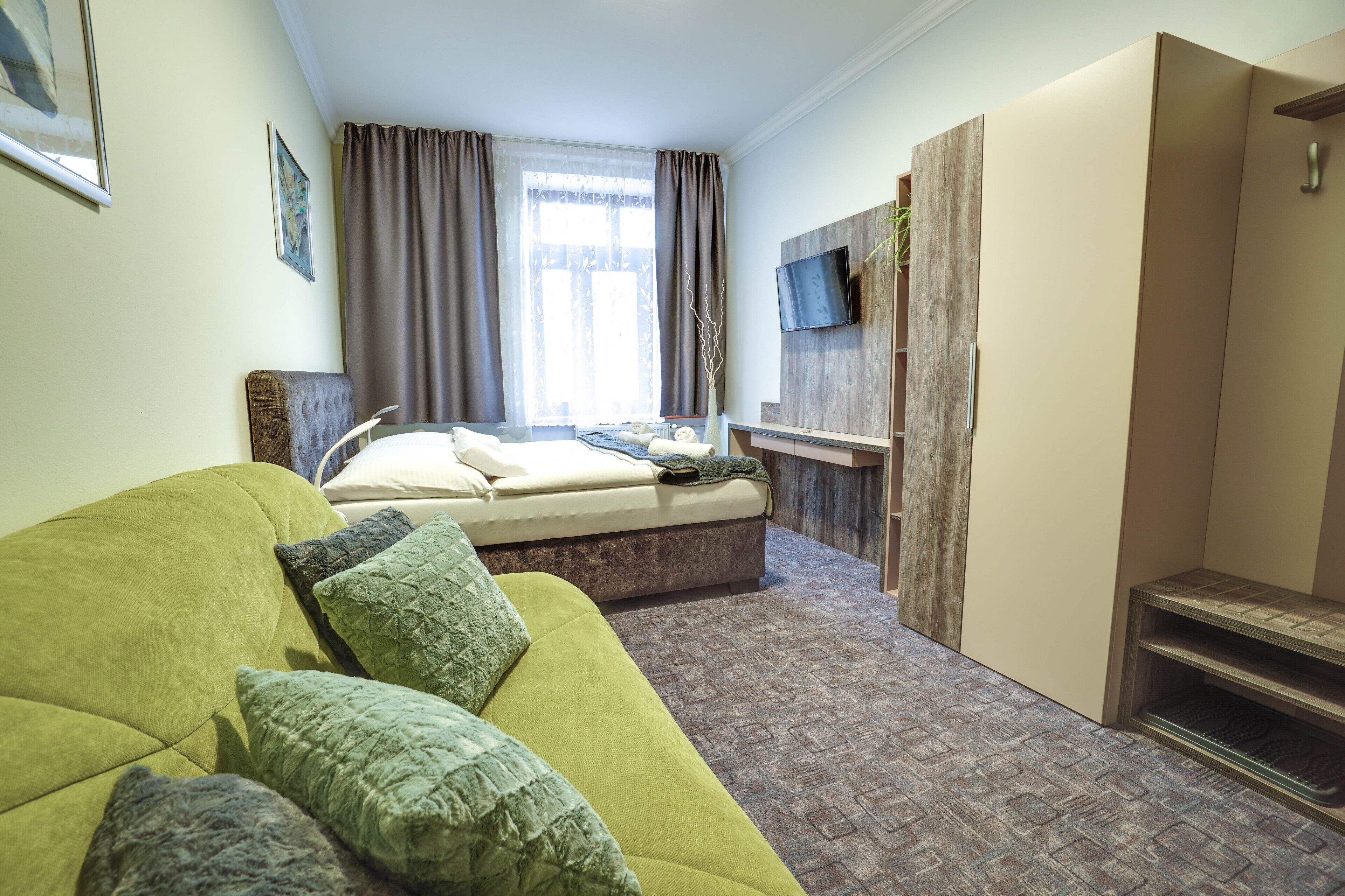 Ein modernes Hotelzimmer mit einem grünen Sofa, einem Bett, einem an der Wand befestigten Fernseher und einem Holzschrank.
