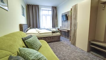 Ein modernes Hotelzimmer mit einem grünen Sofa, einem Bett, einem an der Wand befestigten Fernseher und einem Holzschrank.
