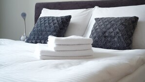 Una cama bien hecha con sábanas blancas y dos almohadas gris oscuro.