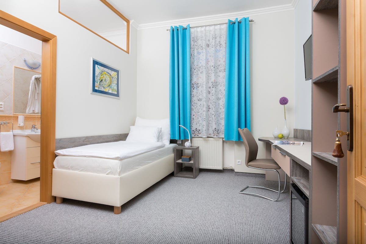 Una habitación de hotel moderna con cama, escritorio, silla y ventana con cortinas.