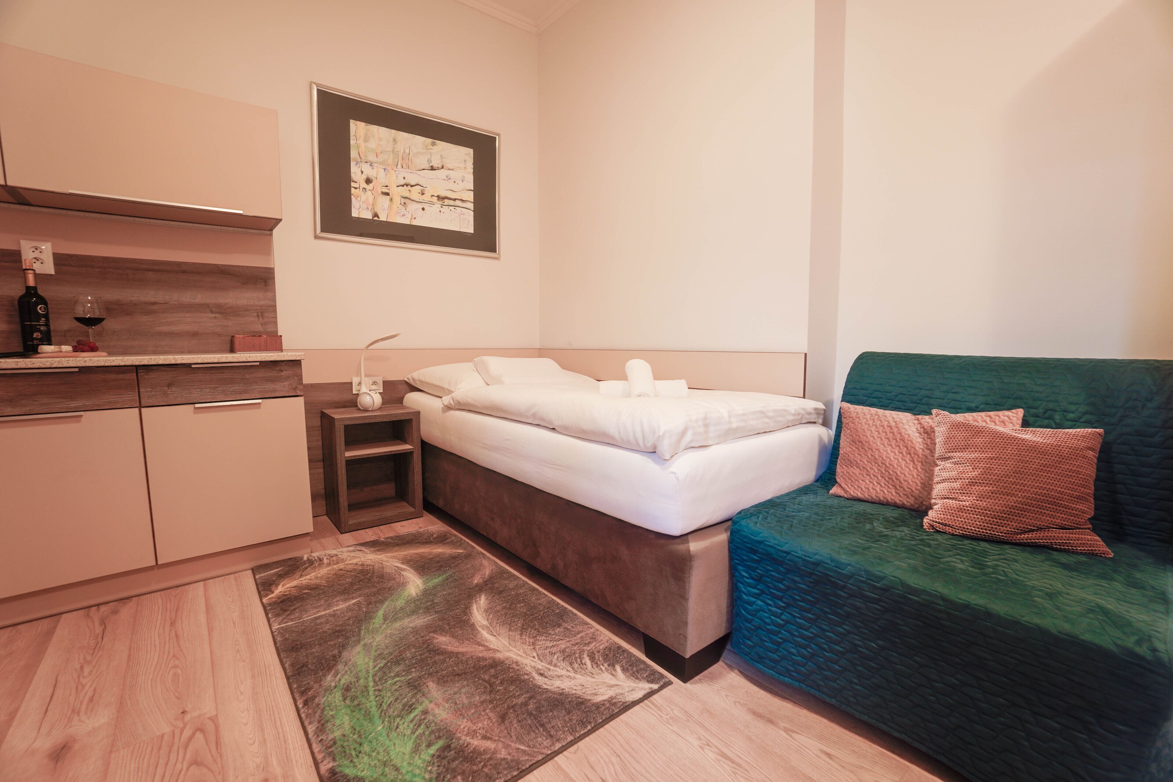 Un dormitorio moderno con cama, sofá verde, mesita de noche con lámpara y un cuadro en la pared.