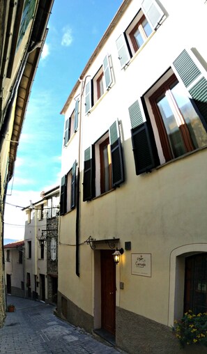 A narrow street with buildings featuring traditional architecture, a sign for 'il Caruglio', and a cobblestone path.