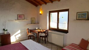 A cozy room with a wooden table, two chairs, a bed with a striped blanket, a radiator, and a window with a view.