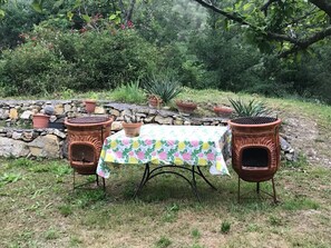 An outdoor patio with terracotta planters, a table with a floral tablecloth, and a stone wall in the background.