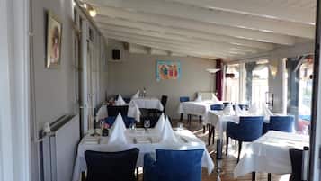 Un restaurant où les tables sont dressées pour le service, avec un mélange de chaises bleues et noires, des nappes blanches et des œuvres d’art encadrées accrochées aux murs.