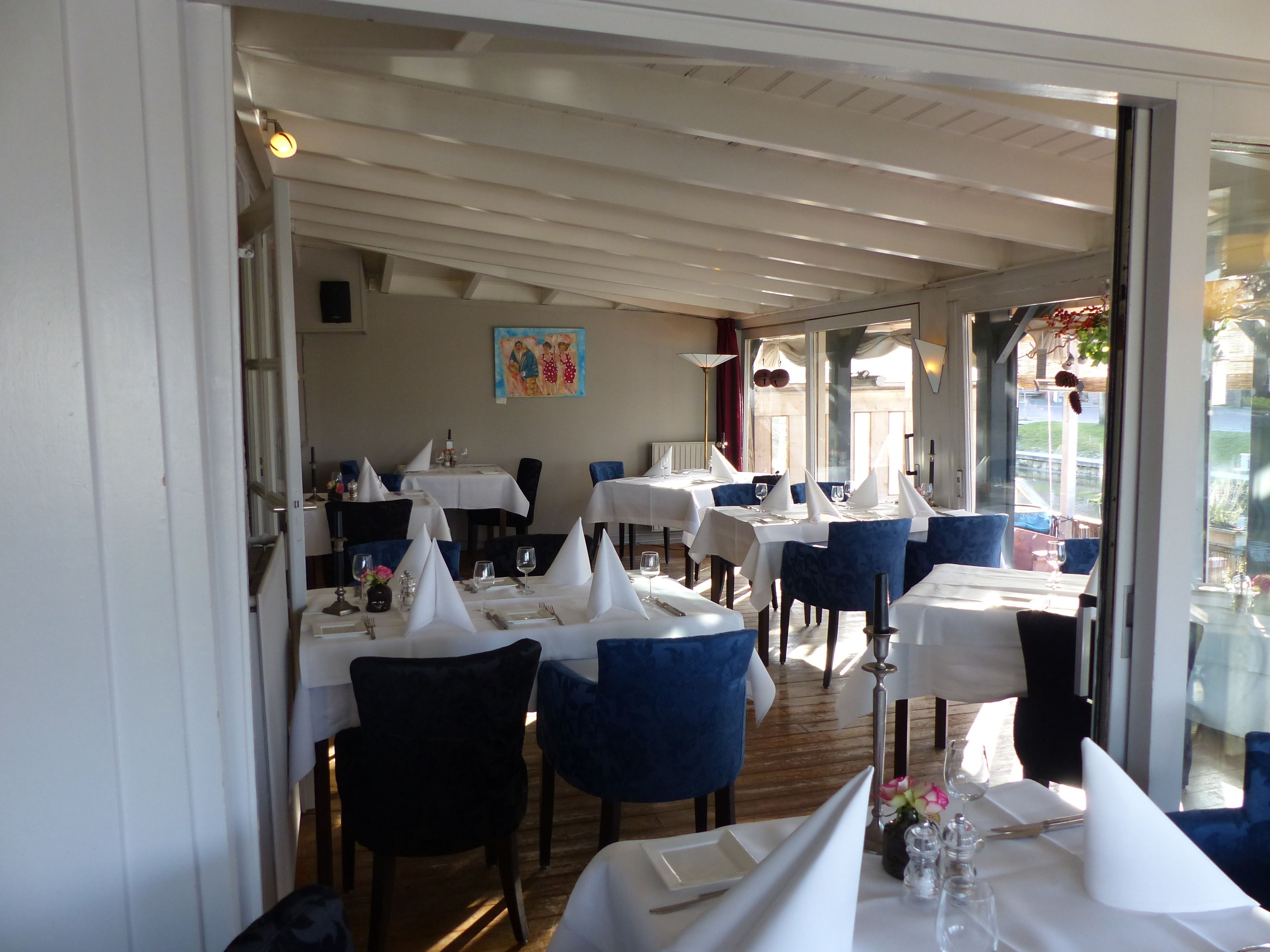 A restaurant with tables set for dining, featuring white tablecloths and blue chairs.