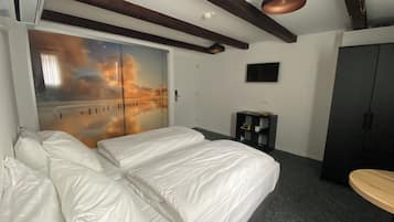 A hotel room with a bed, a wardrobe, a small table, and a wall with a sunset mural.
