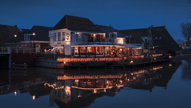 Un edificio frente al agua con un muelle, ventanas iluminadas y un árbol de Navidad.