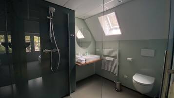 A modern bathroom with a glass shower enclosure, a skylight, a white toilet, and a vanity with a mirror.