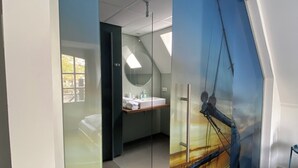 Una habitación de hotel moderna con un ventanal grande, una cama, un baño con lavamanos y espejo, y un diseño de techo original.