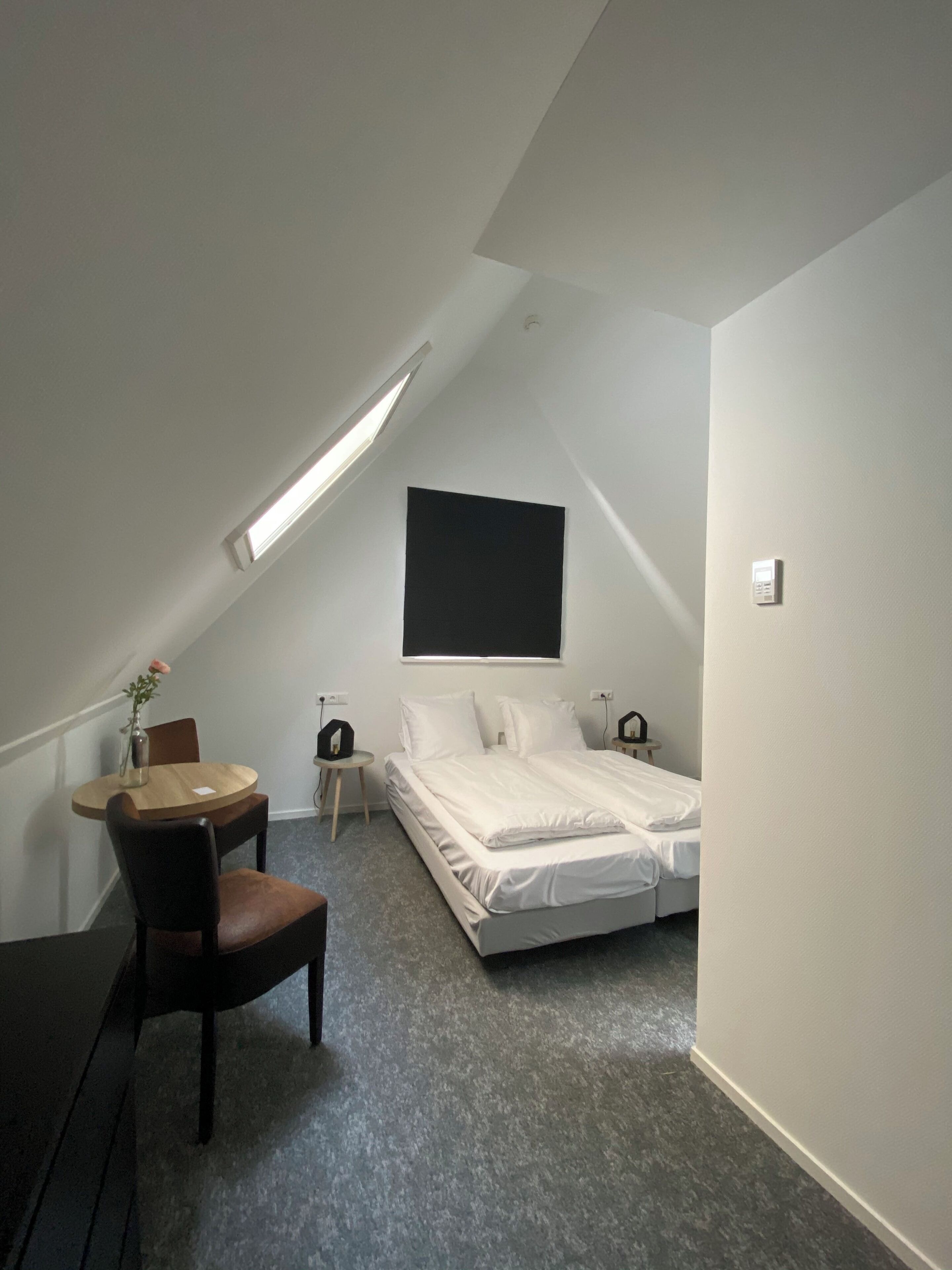 A small, modern bedroom with a sloped ceiling, a single bed, a small table, and a chair.