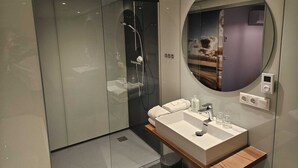Un baño moderno con cabina de ducha de vidrio, tocador con lavamanos y un espejo grande.