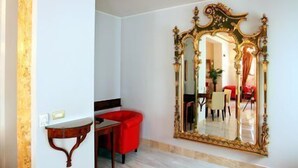 Una habitación con un espejo grande y ornamentado, una silla roja y una mesita.