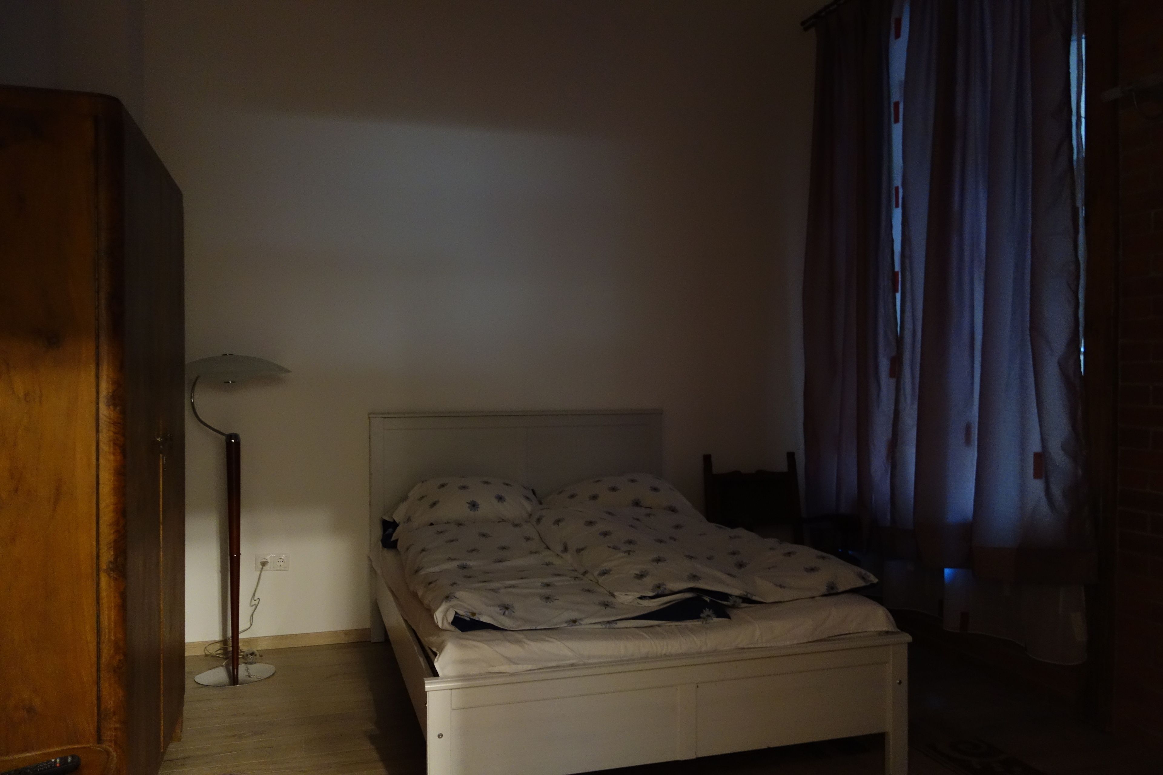 A bedroom with a single bed, a standing lamp, and a wooden wardrobe.