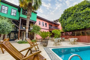 Zona de piscina con sillas de descanso, una piscina y un edificio con varios balcones.