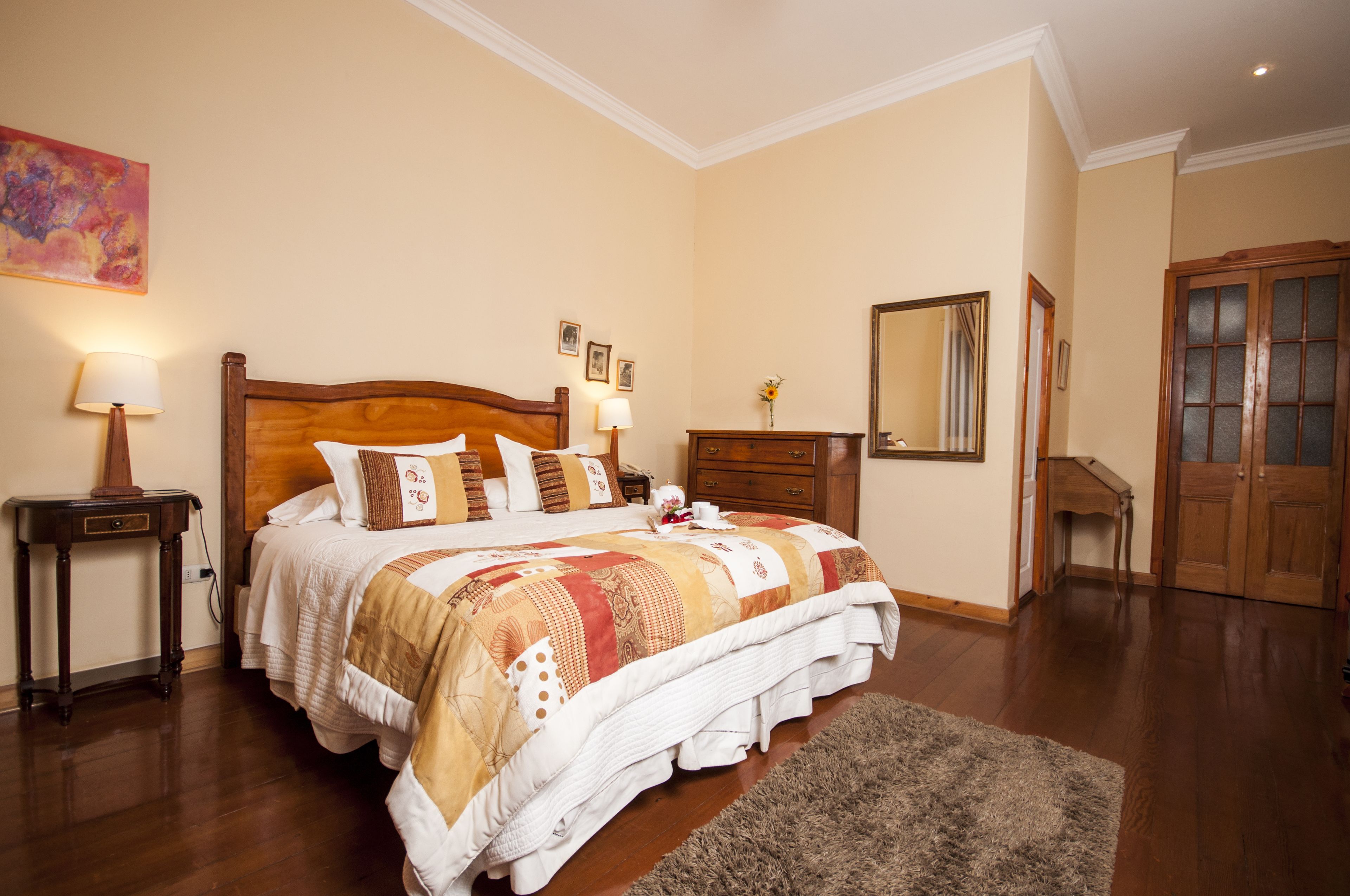A bedroom with a wooden bed, bedside tables with lamps, a dresser, a mirror, and a door.