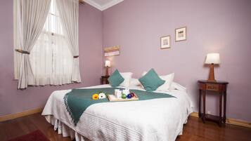 A neatly made bed with a white comforter and green pillows, a bedside table with a lamp, and a window with sheer curtains.