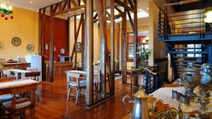 Un comedor con mesas y sillas de madera, una zona de cocina y una escalera que sube a un nivel superior.