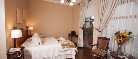 Una habitación de hotel con cama, una silla, una mesa con un jarrón de flores y una ventana con cortinas.