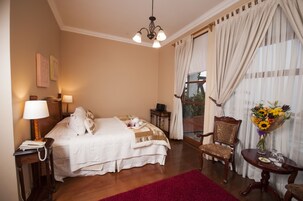 Una habitación de hotel con cama, una silla, una mesa con un jarrón de flores y una ventana con cortinas.