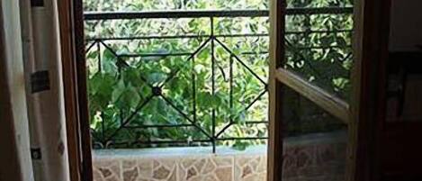 A view through a window with a metal railing, a stone-tiled floor, and greenery outside.