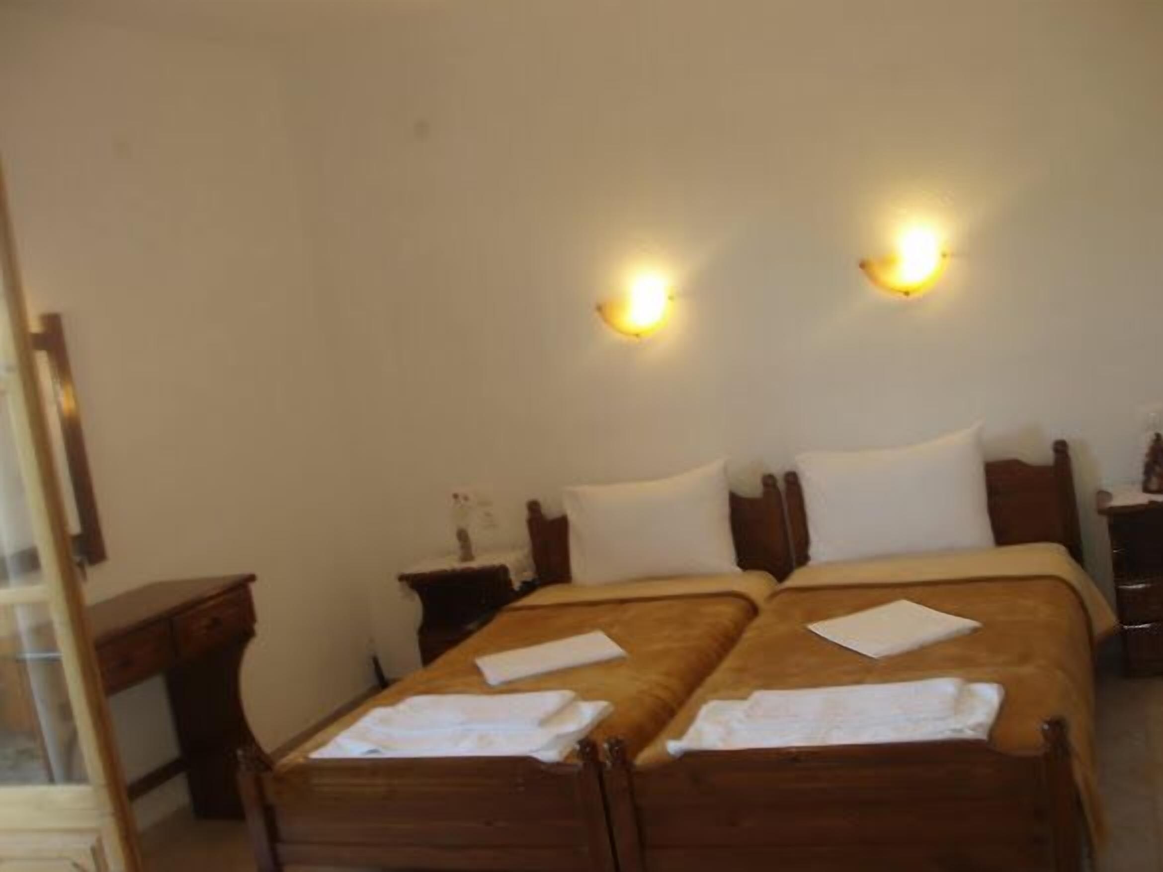Una habitación de hotel con dos camas de madera, mesitas de noche e iluminación en la pared.