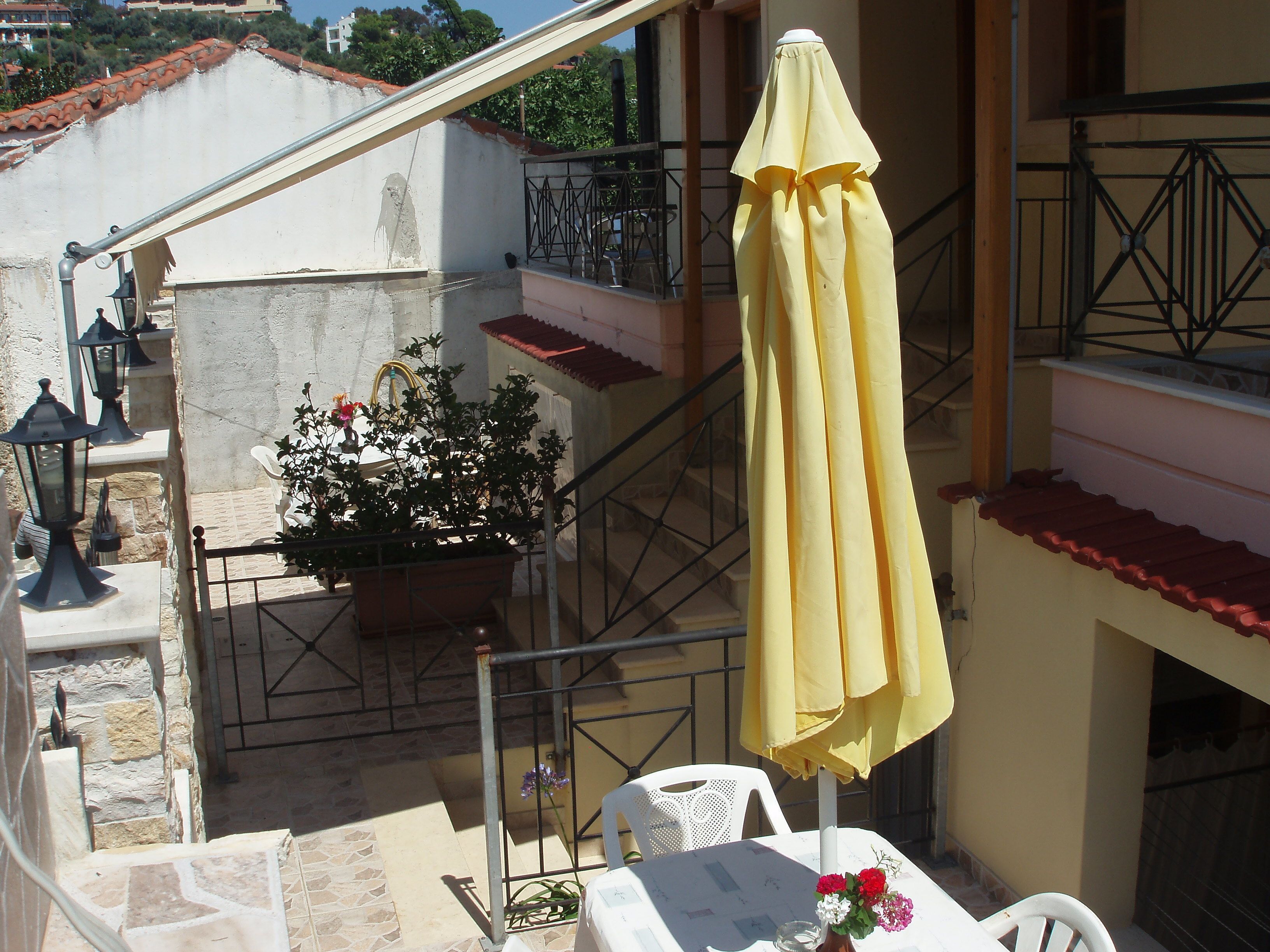A balcony with a yellow umbrella, a potted plant, and a table with a white chair.