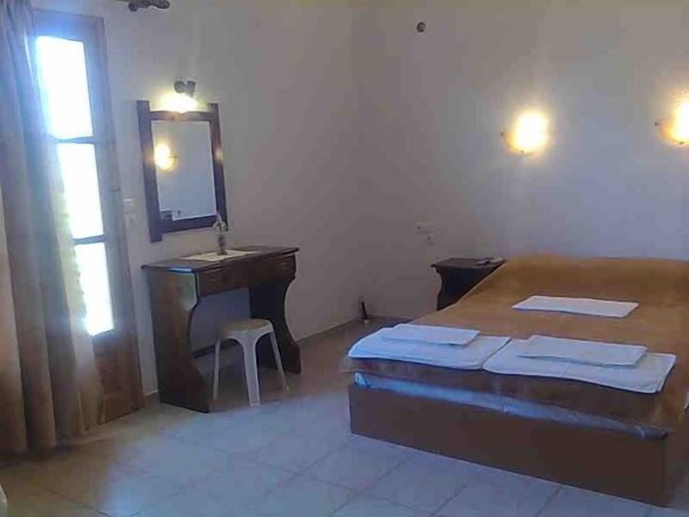 A bedroom with a bed, a desk, a mirror, and a window.