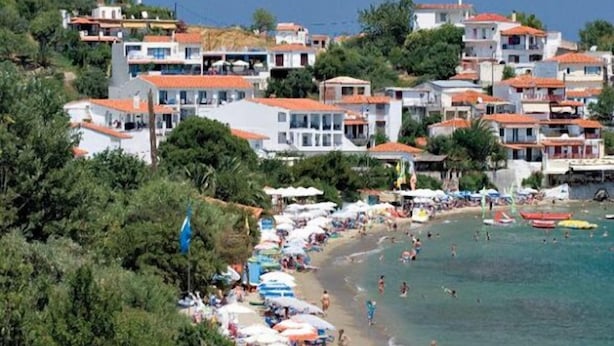 A coastal town with terraced houses, a beach with umbrellas, and people swimming. - Hellen Studios (Skiathos)