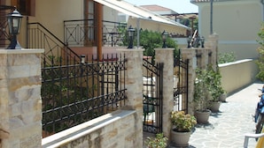 A narrow street with stone walls and metal railings, potted plants, and a parked motorcycle. - Hellen Studios (Skiathos)