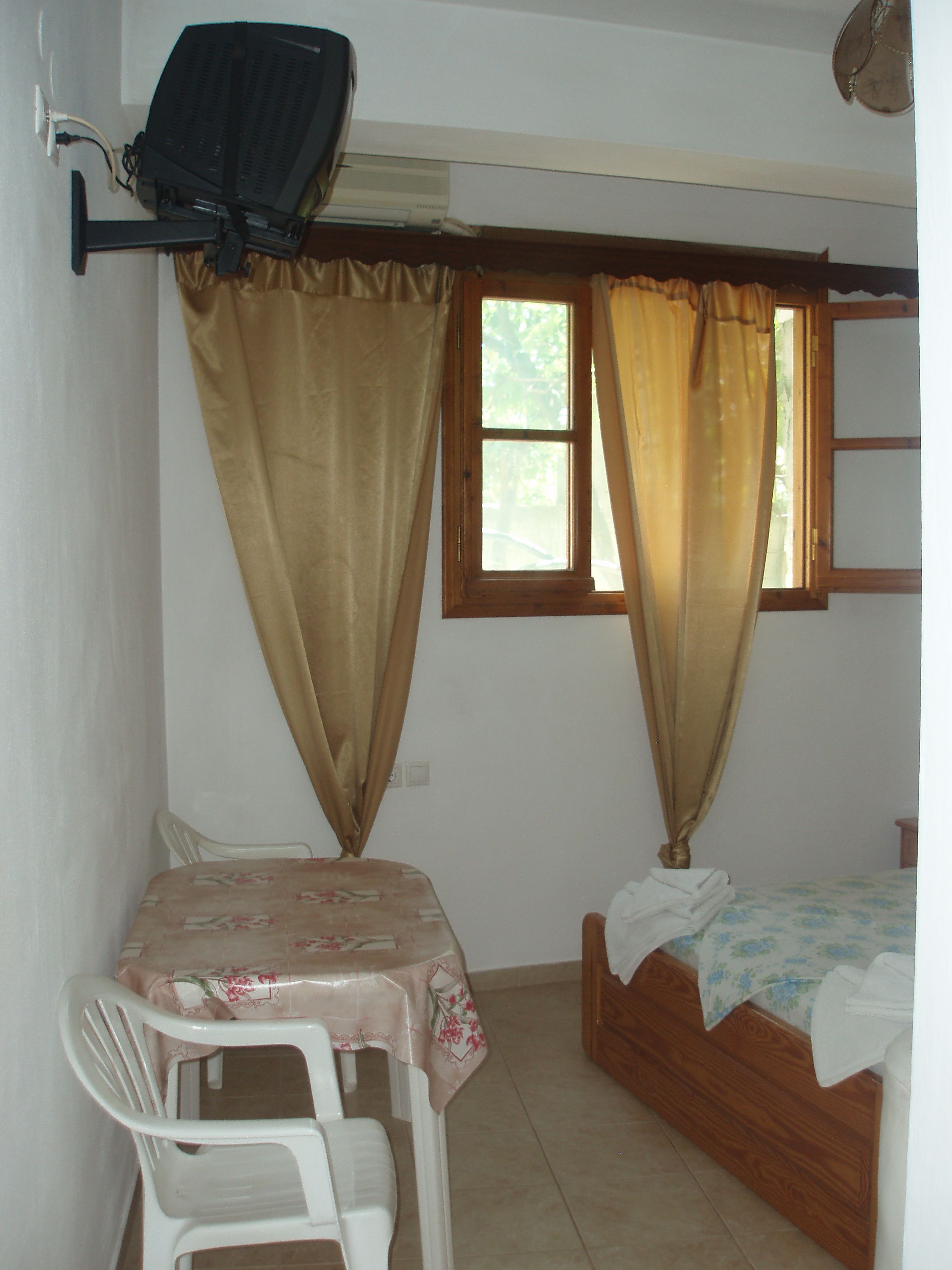 A small room with a single bed, a table with a chair, and a window with curtains.