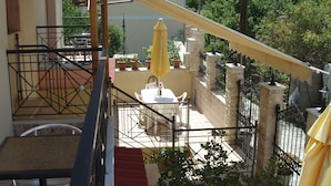 A balcony with a table and chairs, a yellow umbrella, and potted plants. - Hellen Studios (Skiathos)