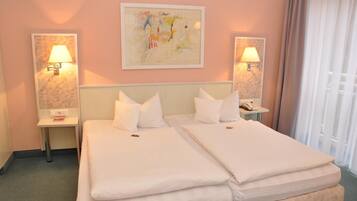 A hotel room with two beds, a nightstand with a lamp, a painting on the wall, and a window with curtains.