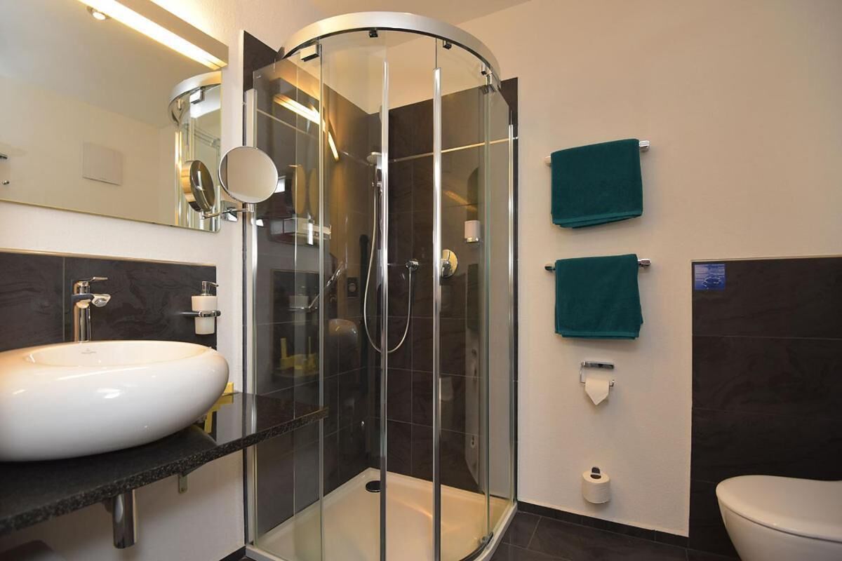 Une salle de bain moderne avec une douche à parois de verre, un lavabo blanc et deux serviettes vertes accrochées au mur.