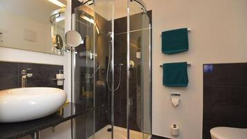 Une salle de bain moderne avec une douche à parois de verre, un lavabo blanc et deux serviettes vertes accrochées au mur.