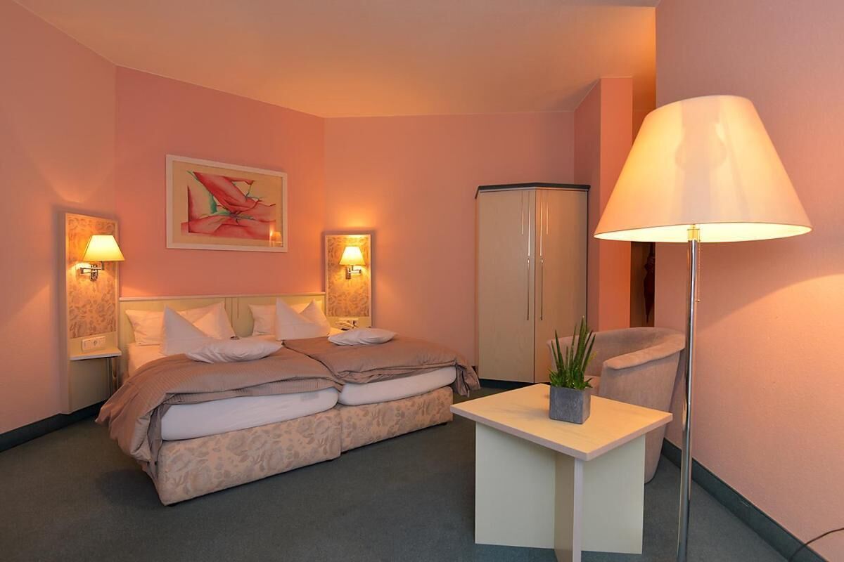 A hotel room with a bed, bedside lamps, a desk with a plant, and a large lamp.