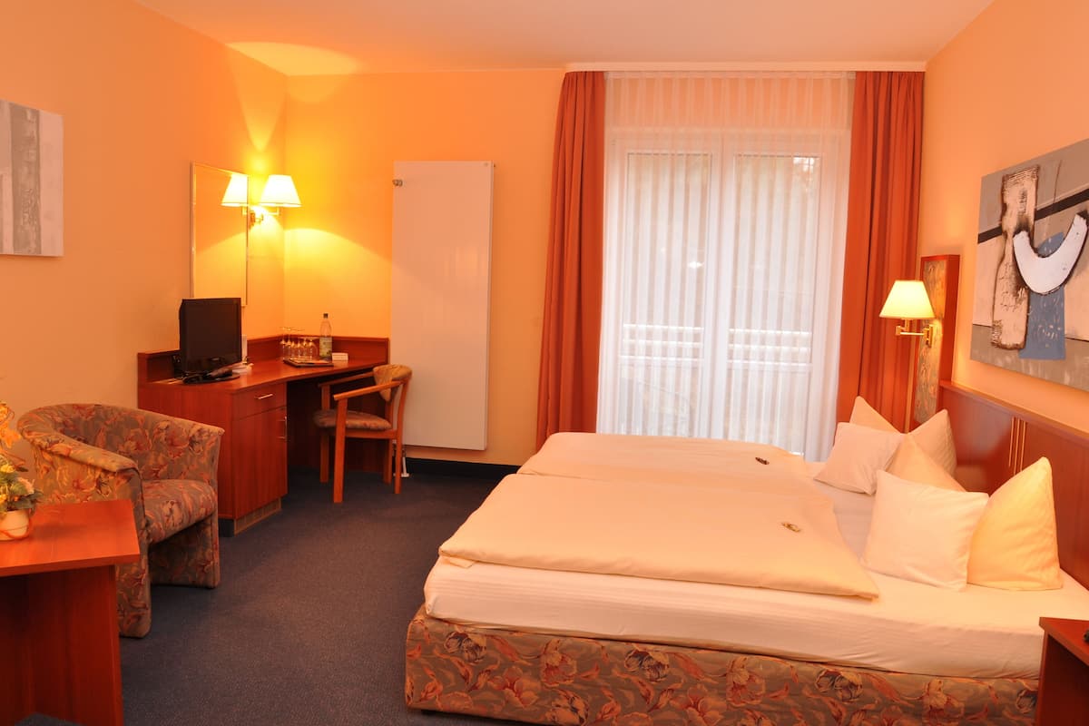 A hotel room with a bed, a desk, a chair, a lamp, and a painting on the wall.