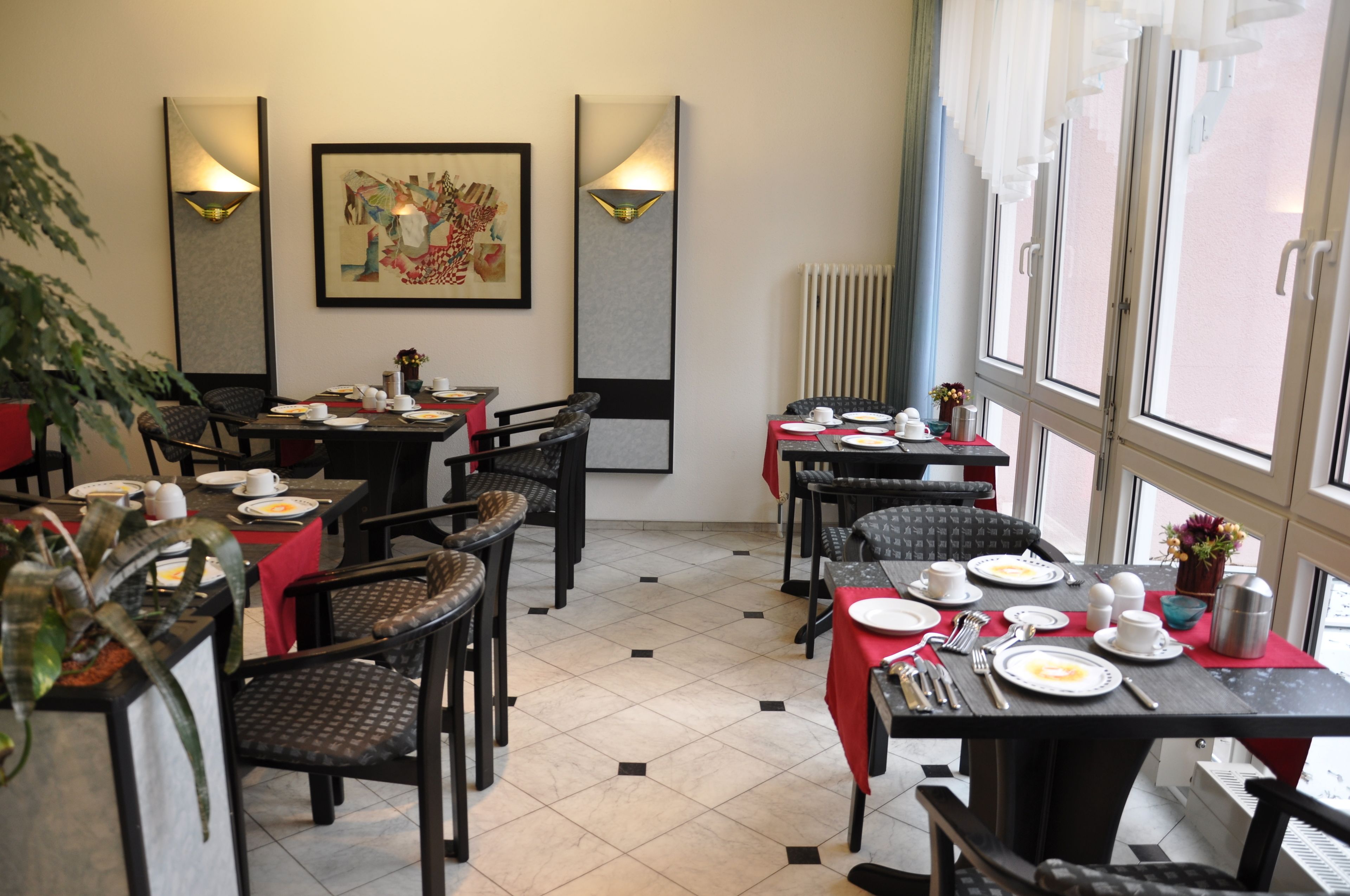 A dining area with tables set for breakfast, featuring chairs, plates, cups, and a large window with a view.