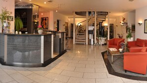 A reception area with a counter, a staircase, and a seating area with a red sofa and a coffee table. - Altstadthotel An Der Werra (Meiningen)