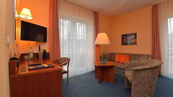 A hotel room with a wooden desk, a television, a sofa, and a chair.