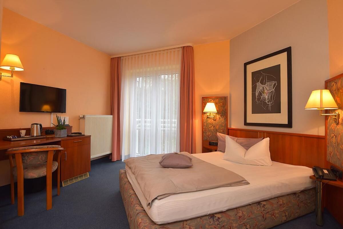 Ein Hotelzimmer mit Bett, Schreibtisch mit Stuhl, Fernseher und einem Fenster mit Vorhängen.