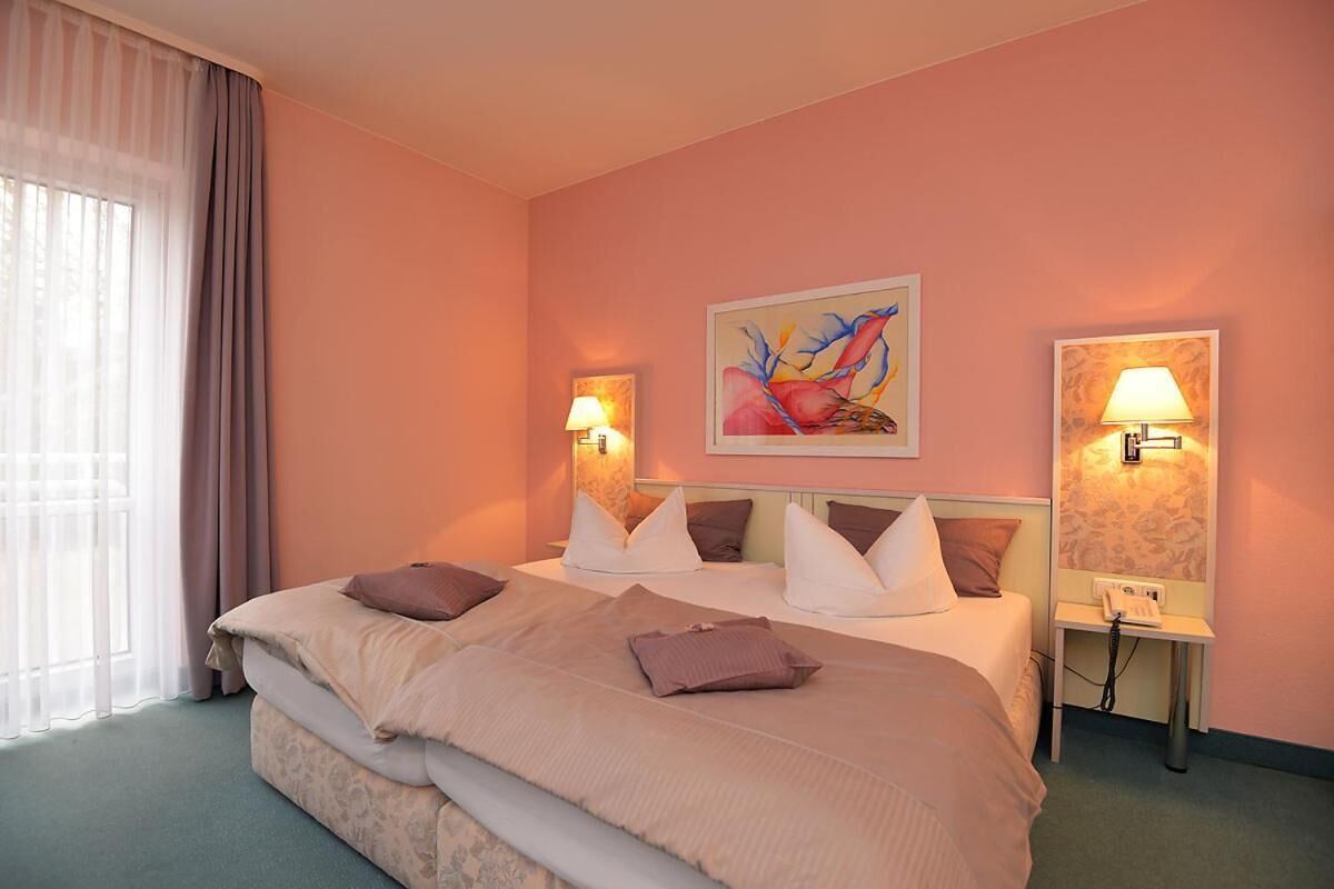 Habitació d'hotel amb un llit gran, dues taules de nit amb làmpades, un quadre a la paret i una finestra amb cortines.