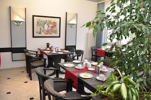 Dine in style with round tables and cushioned chairs, surrounded by artwork and lush greenery.