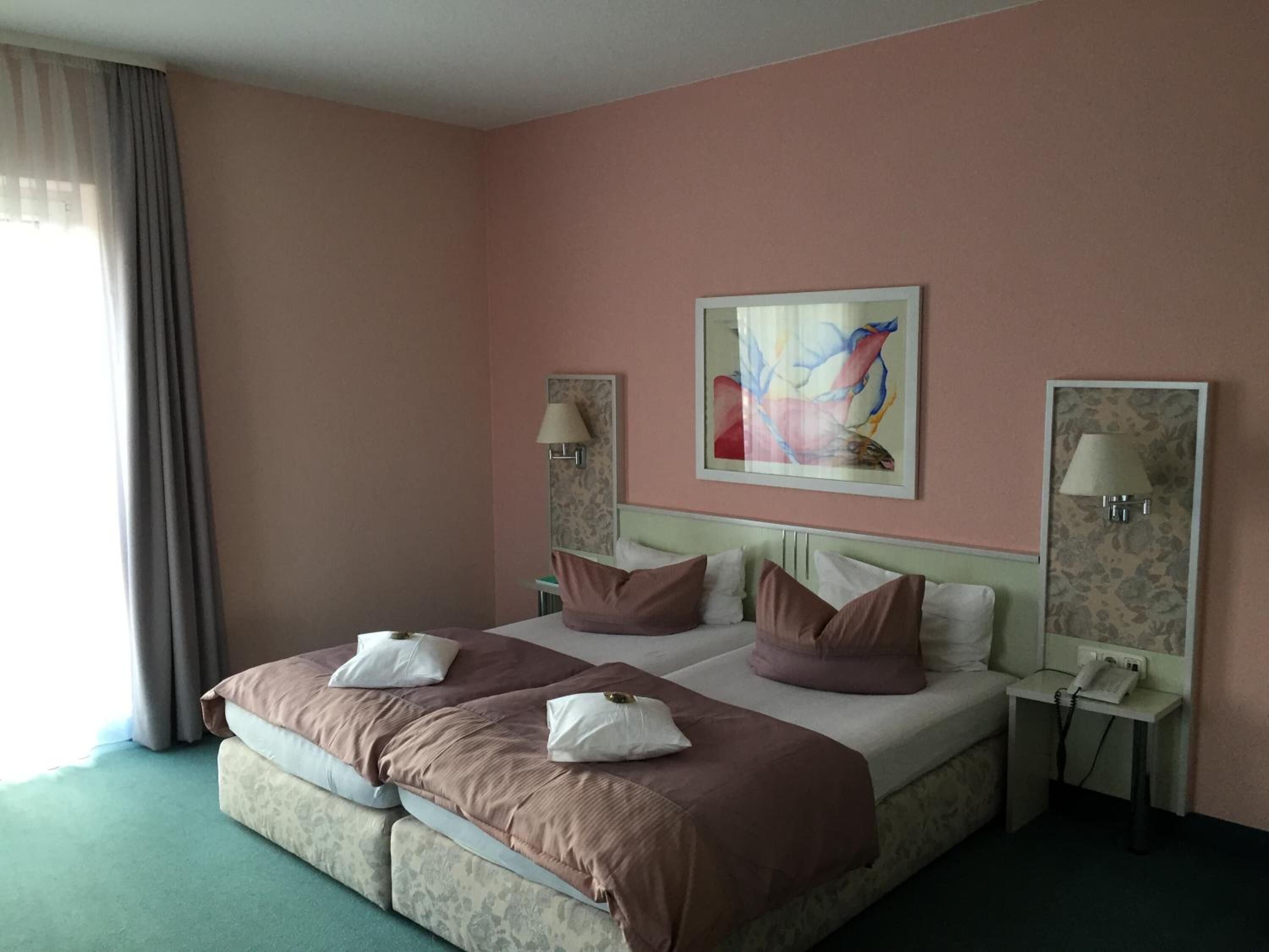 Hotelkamer met een tweepersoonsbed, twee nachtkastjes, een schilderij aan de muur en een raam met gordijnen.