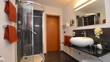 Ein modernes Badezimmer mit einer gläsernen Duschkabine, einem weißen Waschbecken und einem großen Spiegel.