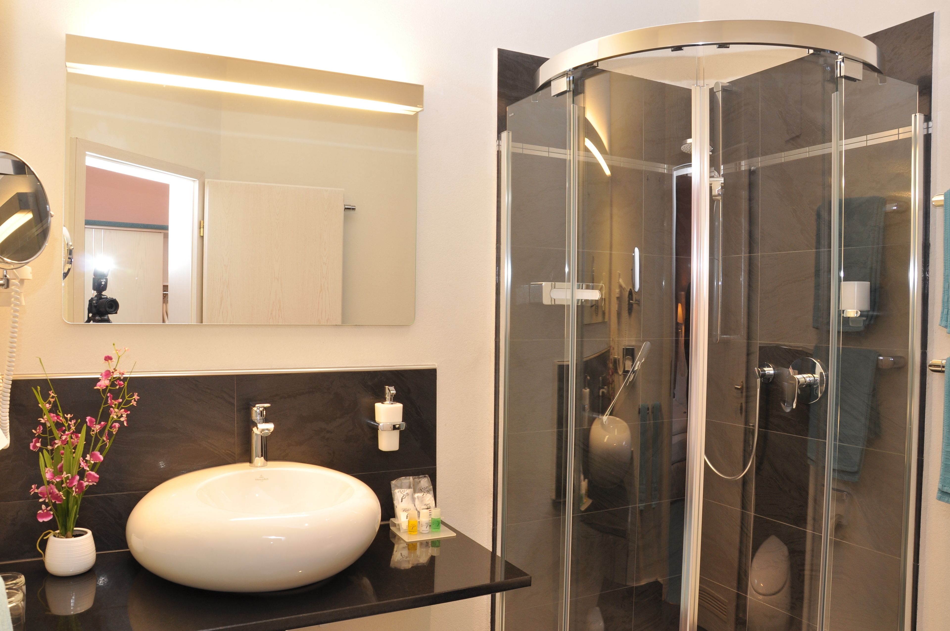 Ein modernes Badezimmer mit einem runden Waschbecken, einer Duschkabine aus Glas und einem Spiegel über dem Waschbecken.