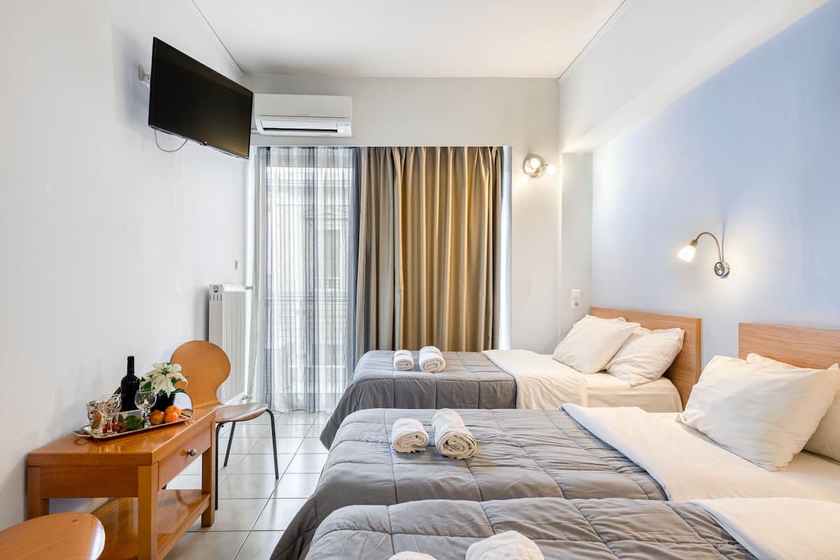 Quarto de hotel com duas camas, uma mesa de trabalho com cadeira, televisão e janela com cortinas.