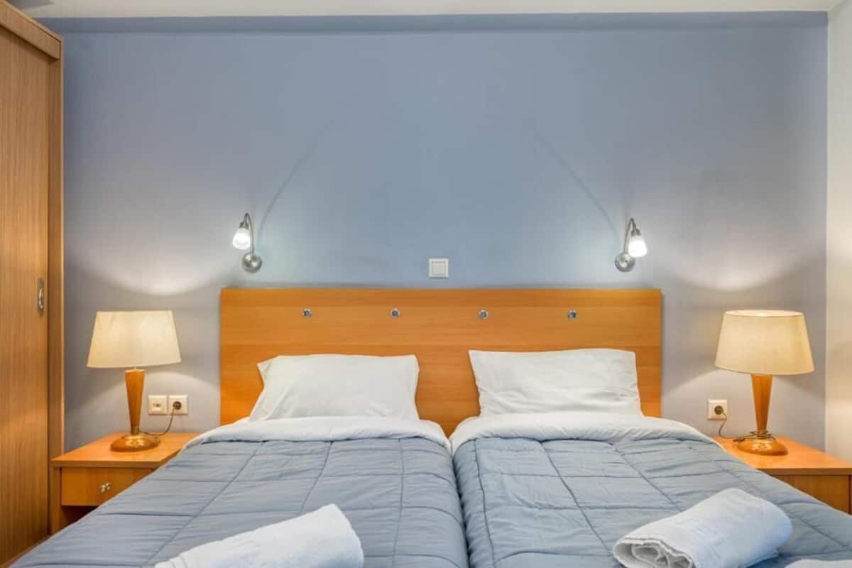 Uma cama de casal com cabeceira de madeira, duas luminárias de cabeceira e uma parede azul.