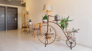 A modern hotel lobby with a vintage bicycle wheel table holding potted plants, a wooden chair, and a table with a lamp. - Diros Hotel (Athens)